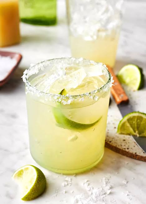 A lime cocktail over ice with a salted rim and fresh lime wedges
